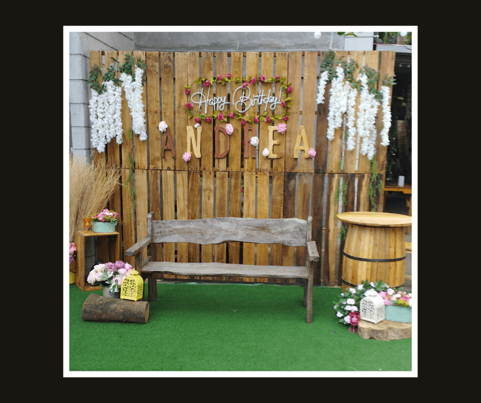 Tall rustic slat wall with cascading white flowers, warm lettering, and a wooden bench