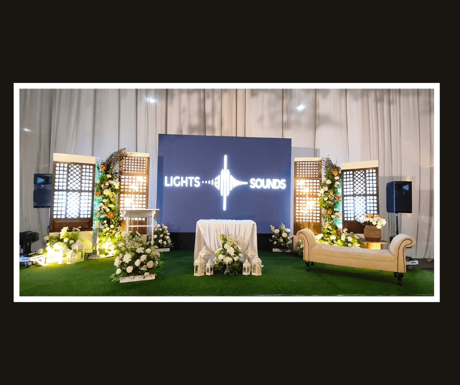 Corporate backdrop styling with illuminated lattice panels, greenery, flowers, and presentation screens