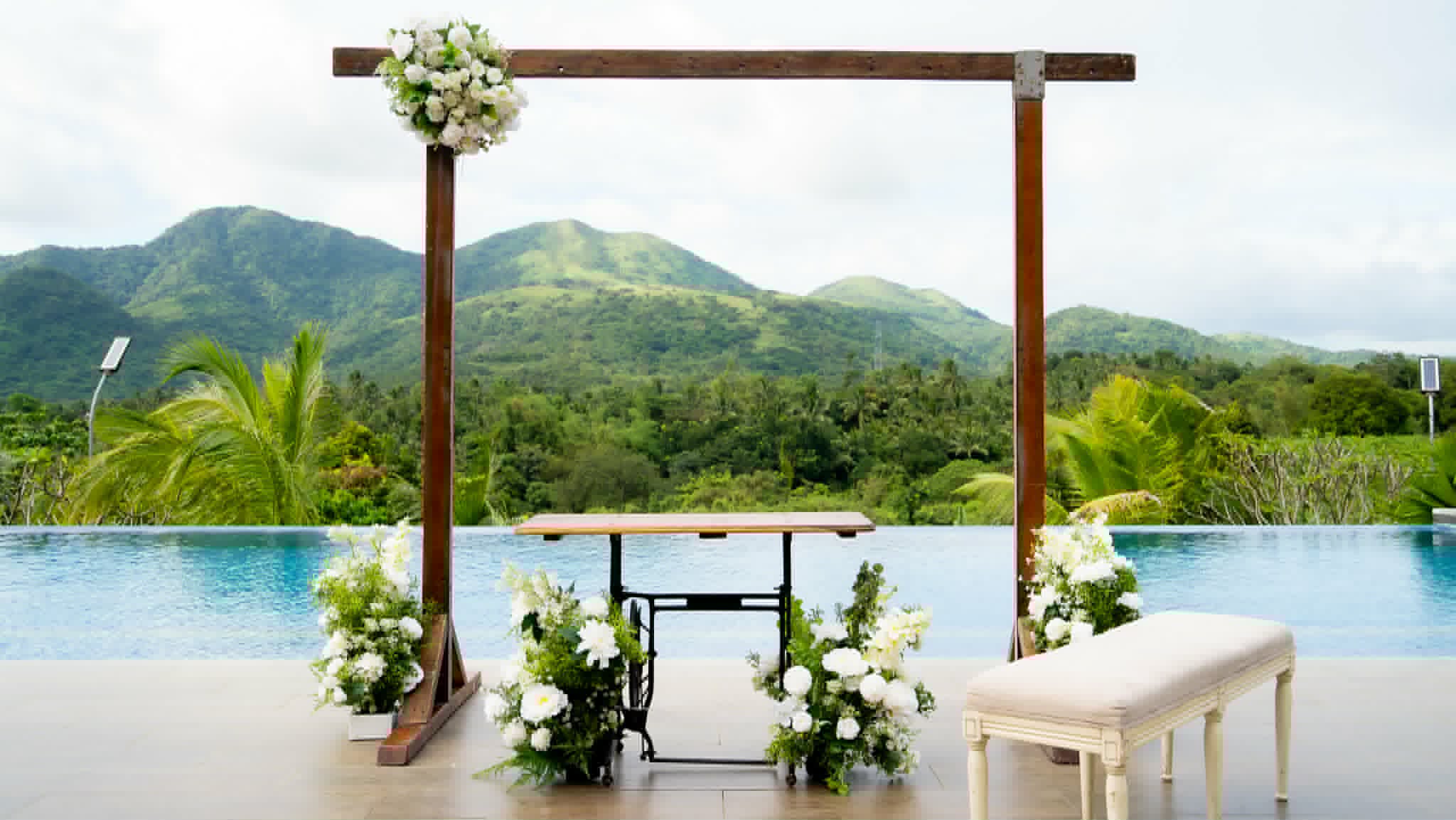 Simple dark wood ceremony frame overlooking a pool and mountain landscape