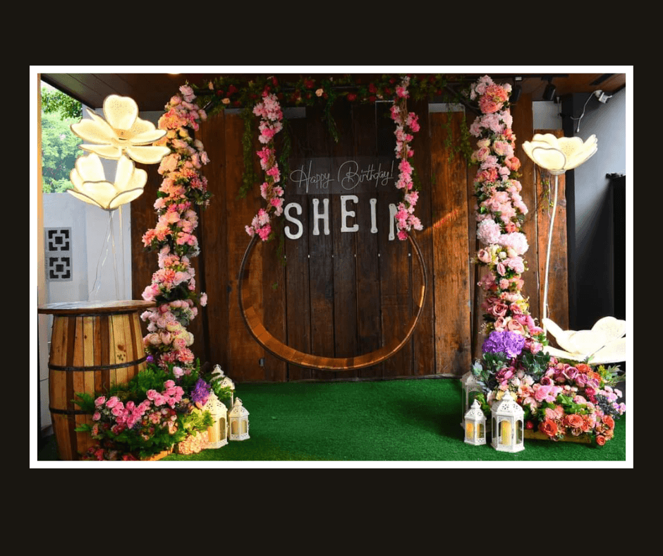 Dark rustic plank wall framed by a crescent of pink flowers and greenery