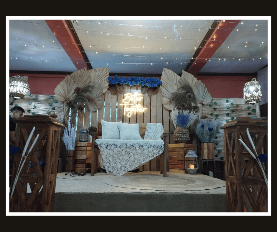 Styled backdrop with frosted palm leaves, pale flowers, timber panels, and warm script lighting