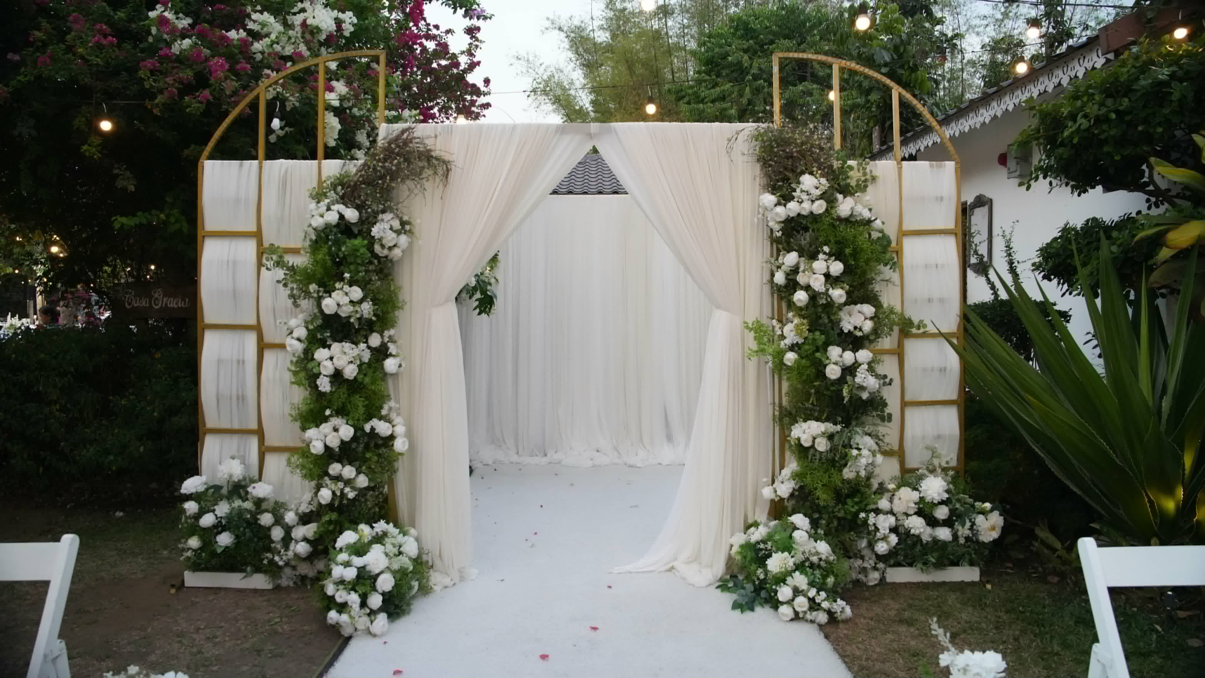Gold rectangular frame surrounding white drapery and floral ceremony arrangements