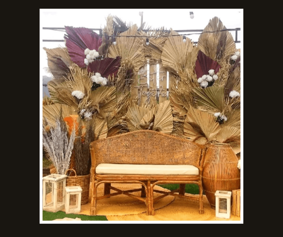 Layered dried palm leaf backdrop with burgundy accents and a woven bench