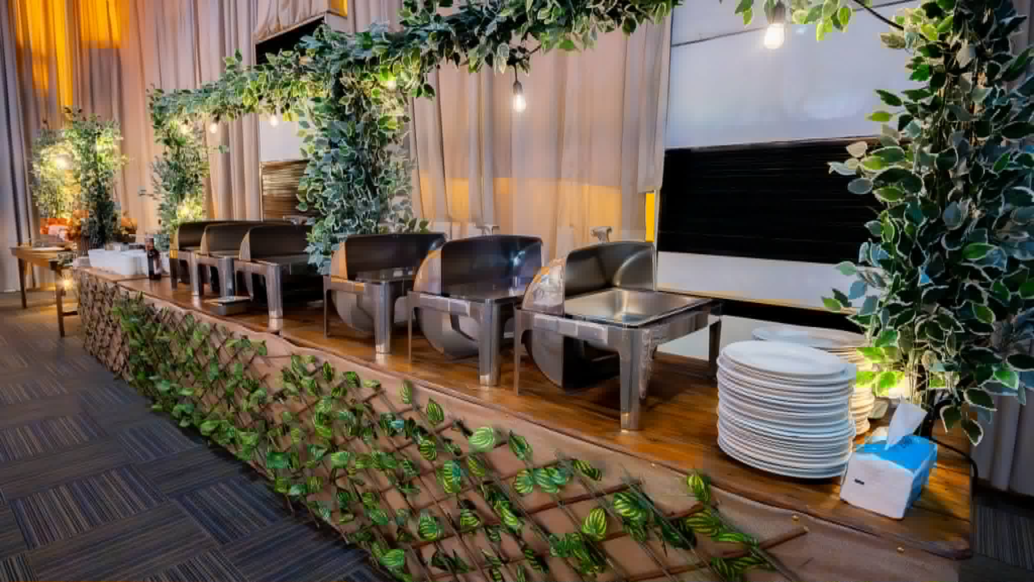 Elevated lounge stage with dark seating, greenery, drapery, and presentation screens