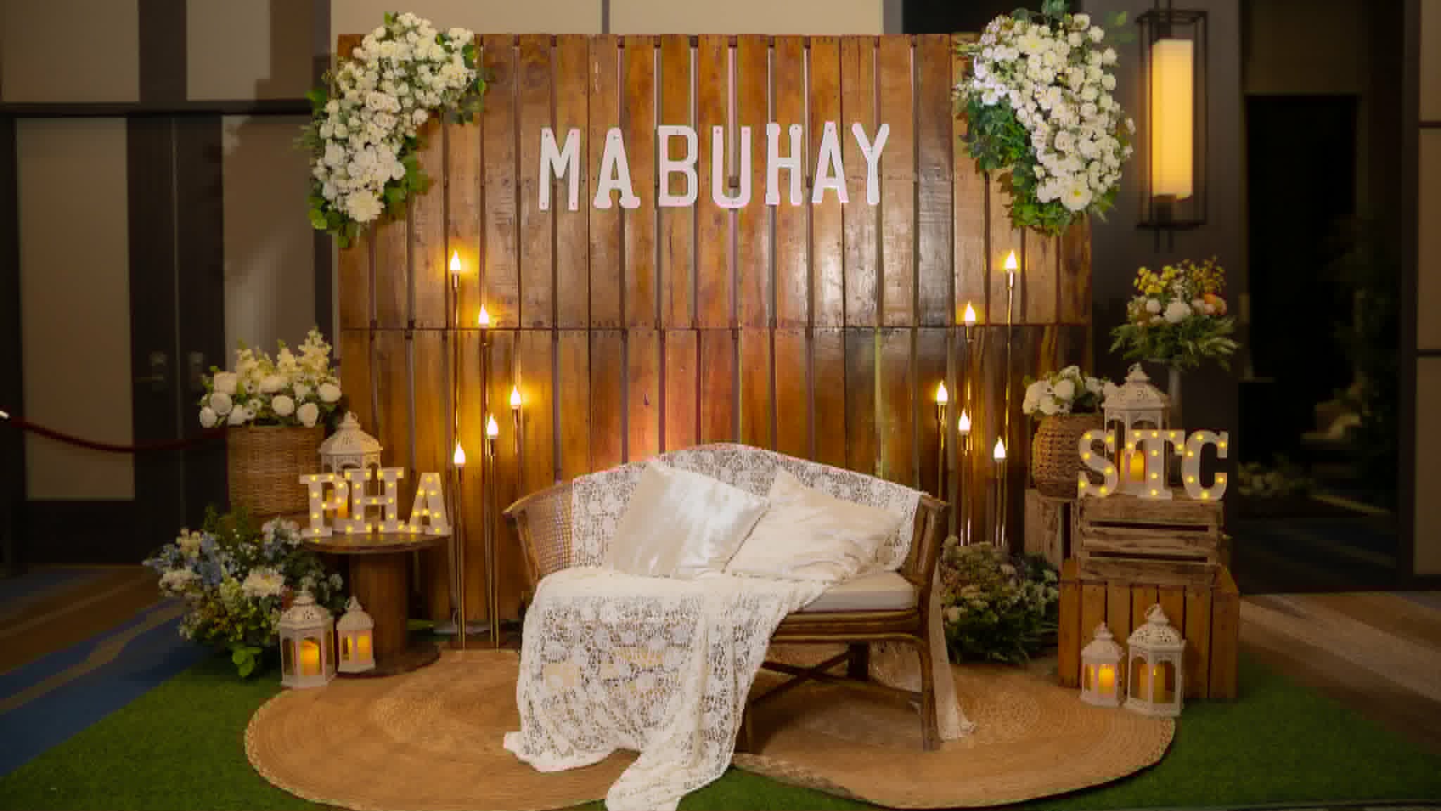 Mabuhay rustic wood backdrop with floral corners, lanterns, and lounge seating