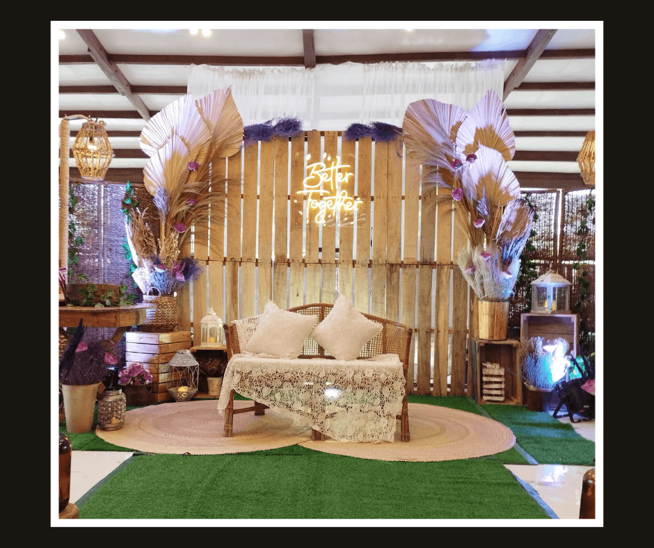 Curved timber slat wall with pampas grass, pale tropical leaves, lanterns, and a cream loveseat