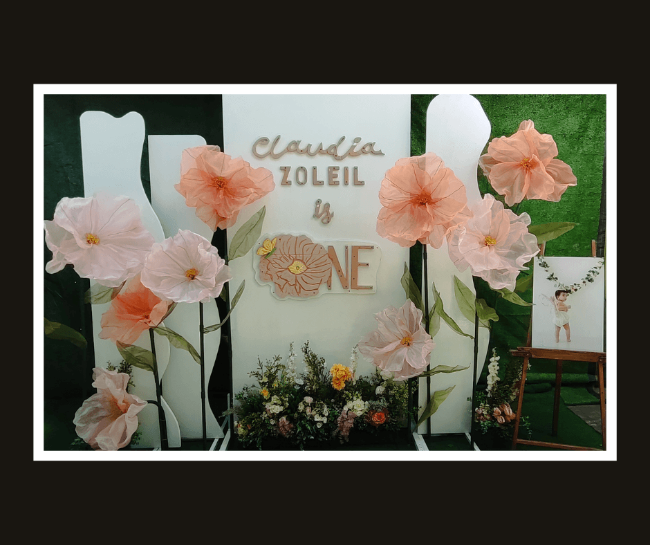 White name backdrop decorated with oversized peach paper flowers and dark green leaves