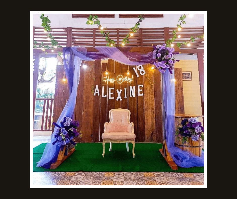Rustic rectangular frame with purple drapery, flowers, warm bulbs, and a blush chair