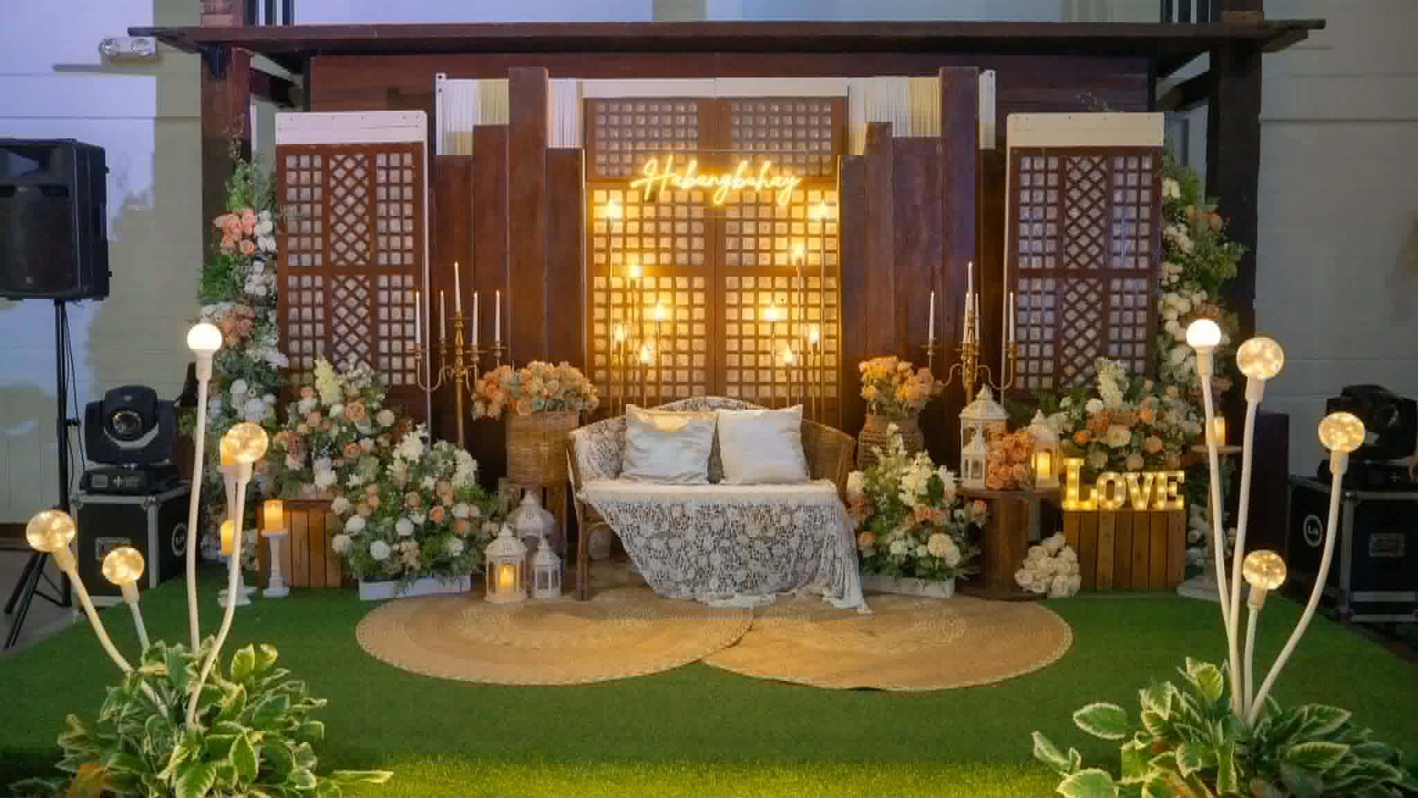 Rustic capiz-panel stage with florals, warm lights, seating, and event lettering