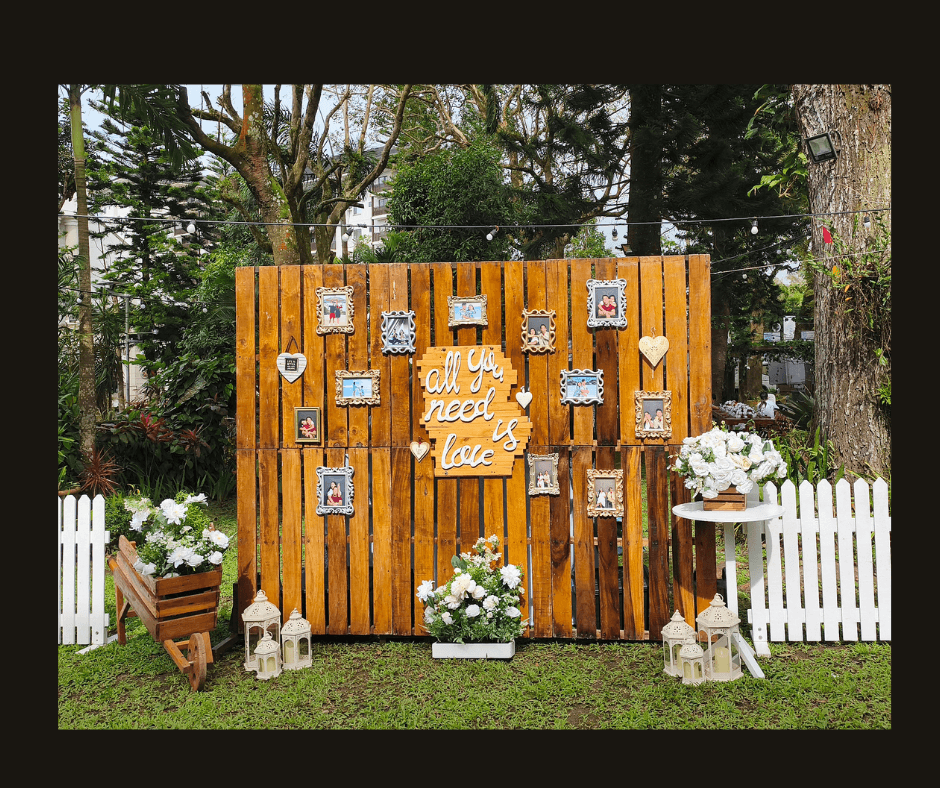 Outdoor rustic love-note wall with hanging cards, painted hearts, white flowers, and lanterns