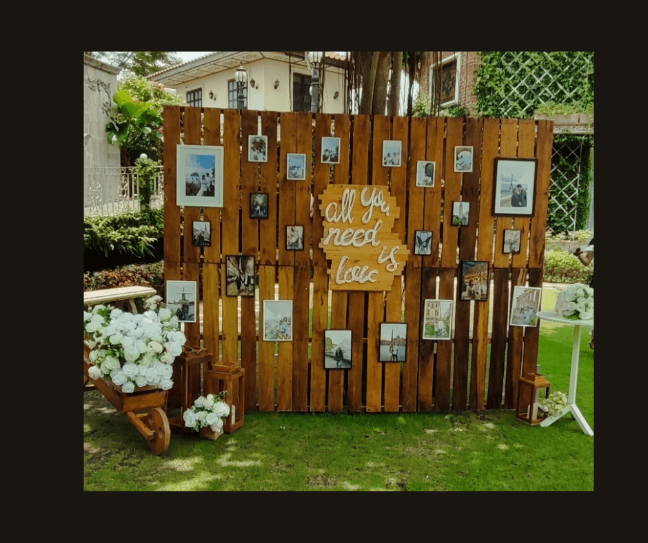 Outdoor timber photo gallery wall with hanging snapshots, hearts, flowers, and a love sign