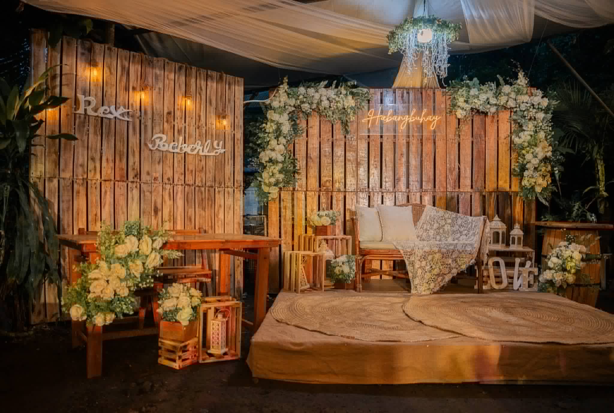 Rustic wooden platform stage with plank wall, greenery, hanging decor, and vintage props