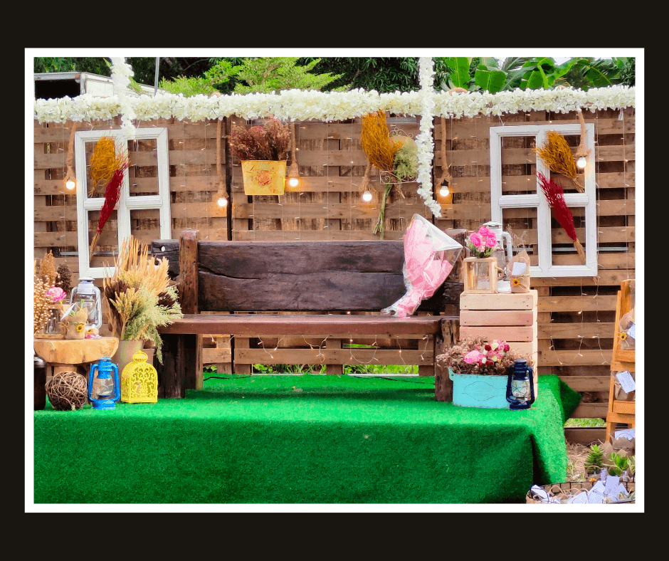 Rustic pallet wall with two white window frames, hanging flowers, and a wooden bench