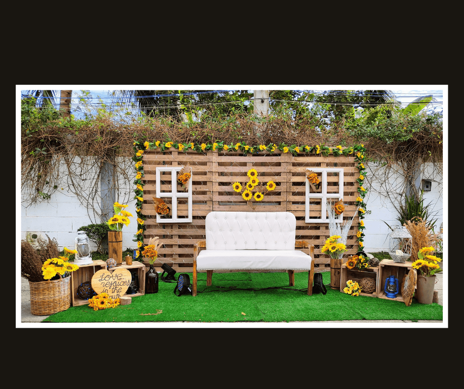 Rustic pallet lounge backdrop with sunflowers, greenery, lanterns, and a white loveseat