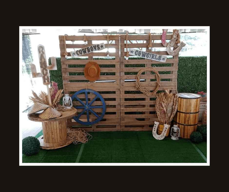 Rustic pallet backdrop decorated with wagon wheels, rope, a horseshoe, barrel, and western props