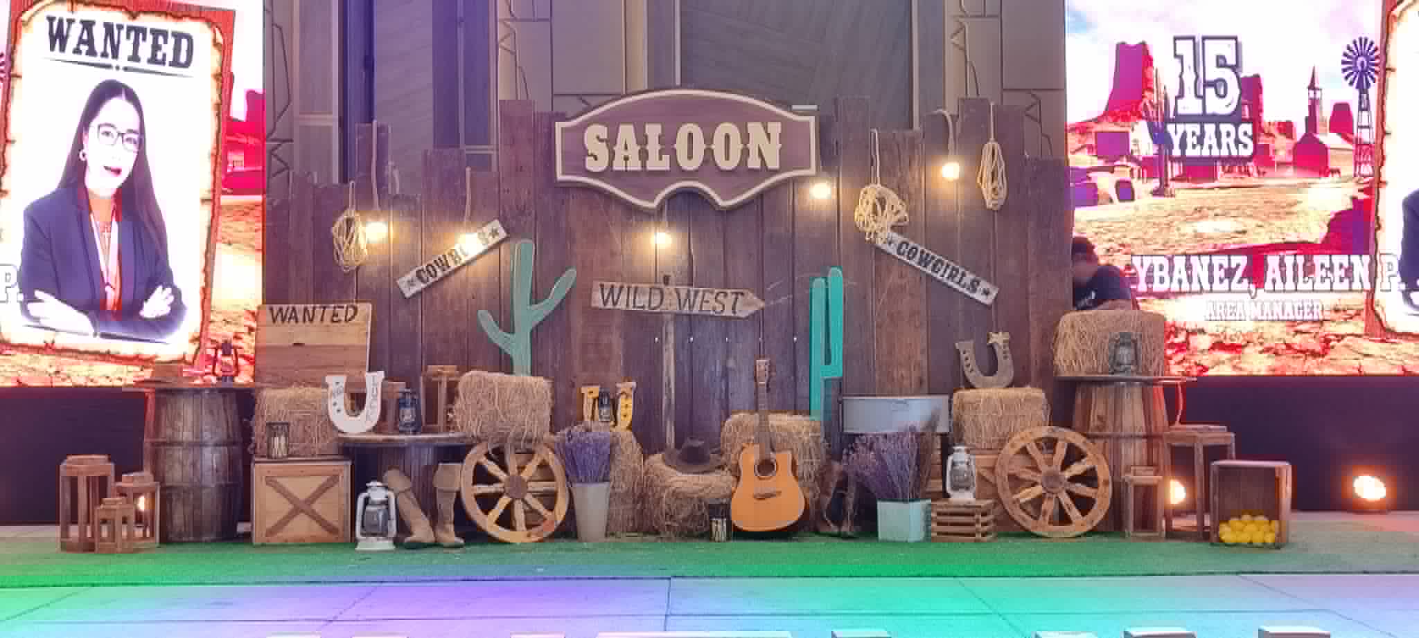 Large western saloon stage backdrop with wagon wheels, guitars, and themed posters