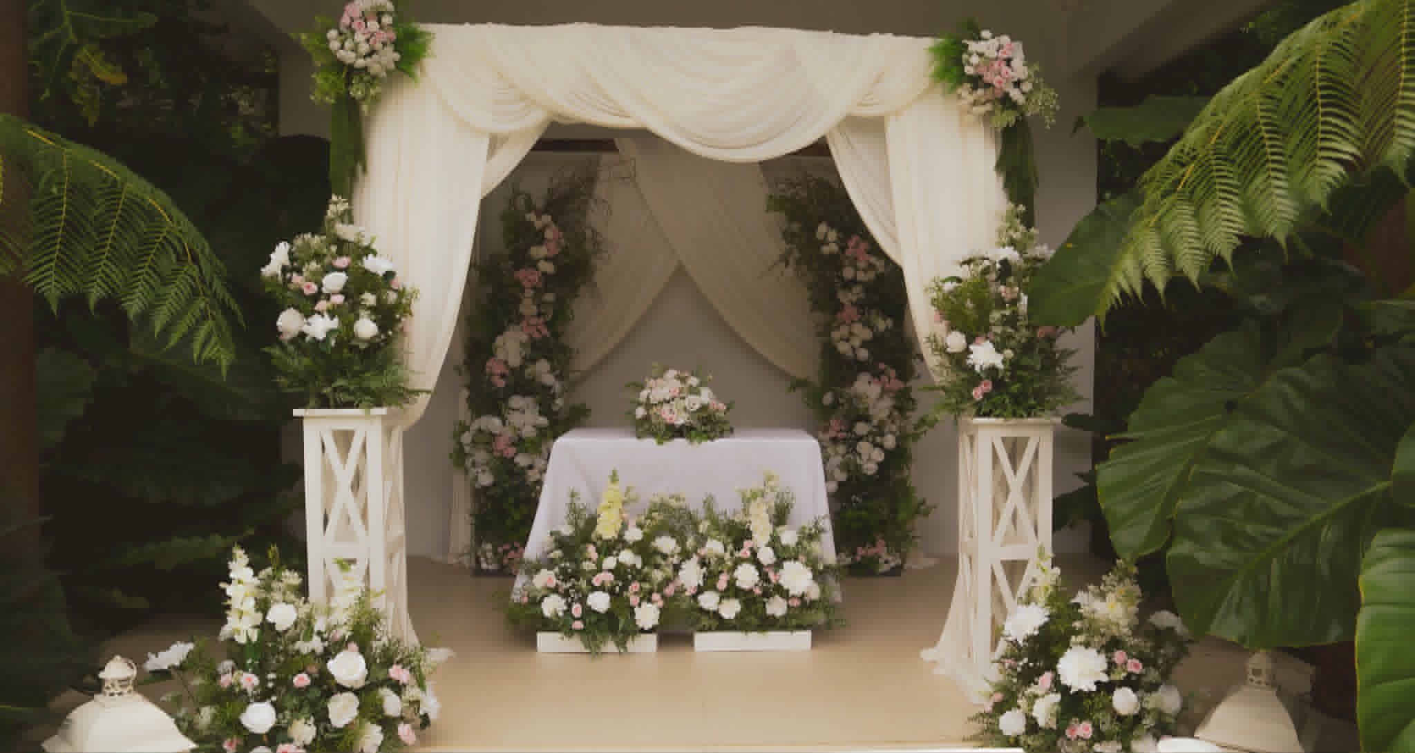 Small white draped ceremony nook with white flowers and greenery