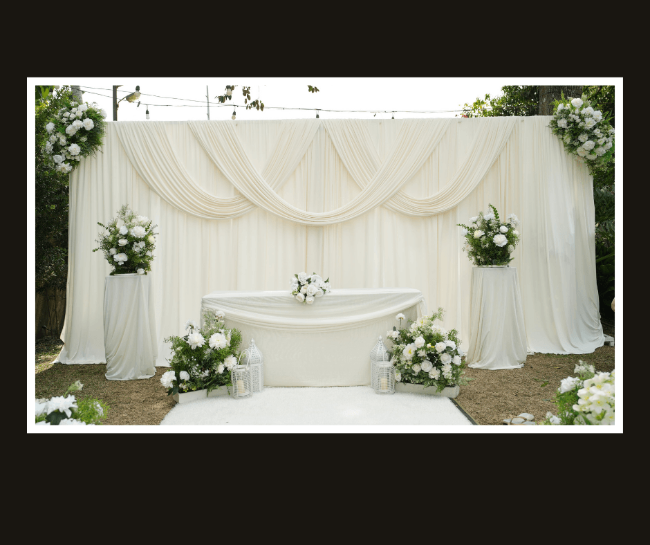 White draped ceremony wall with symmetrical flowers, hanging greenery, and a white signing table
