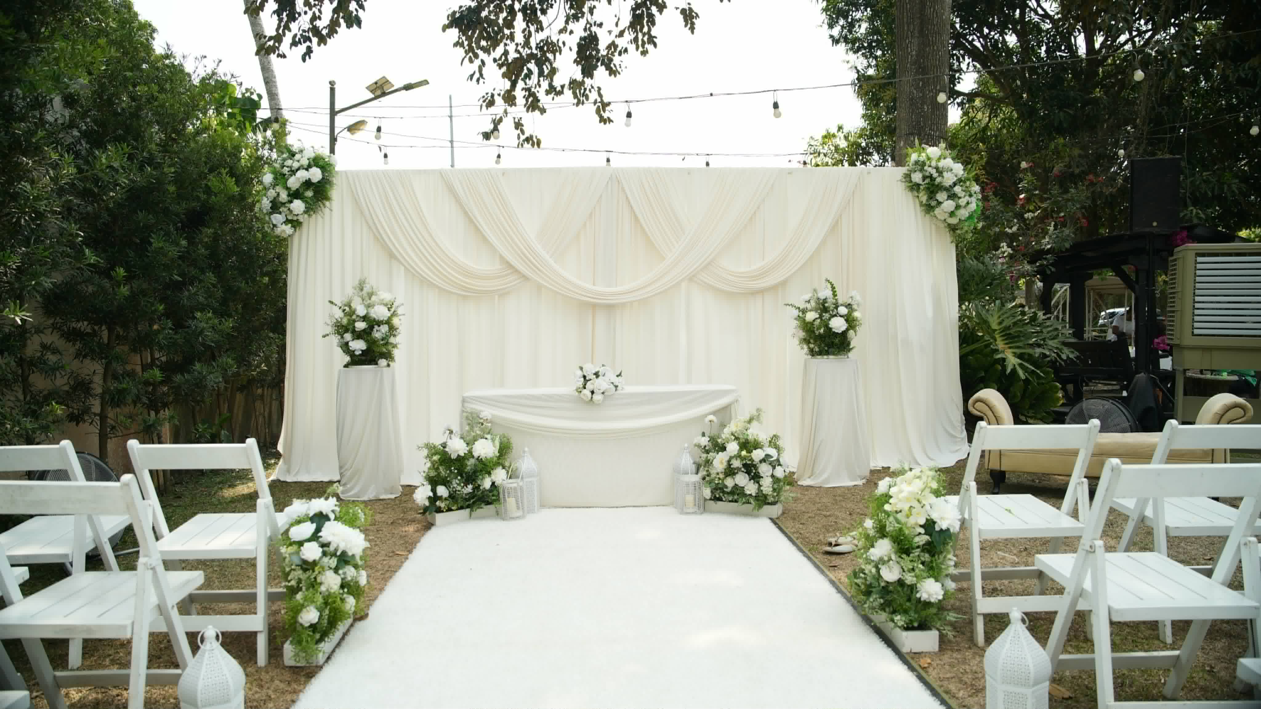 White draped ceremony backdrop with floral arrangements and white chairs