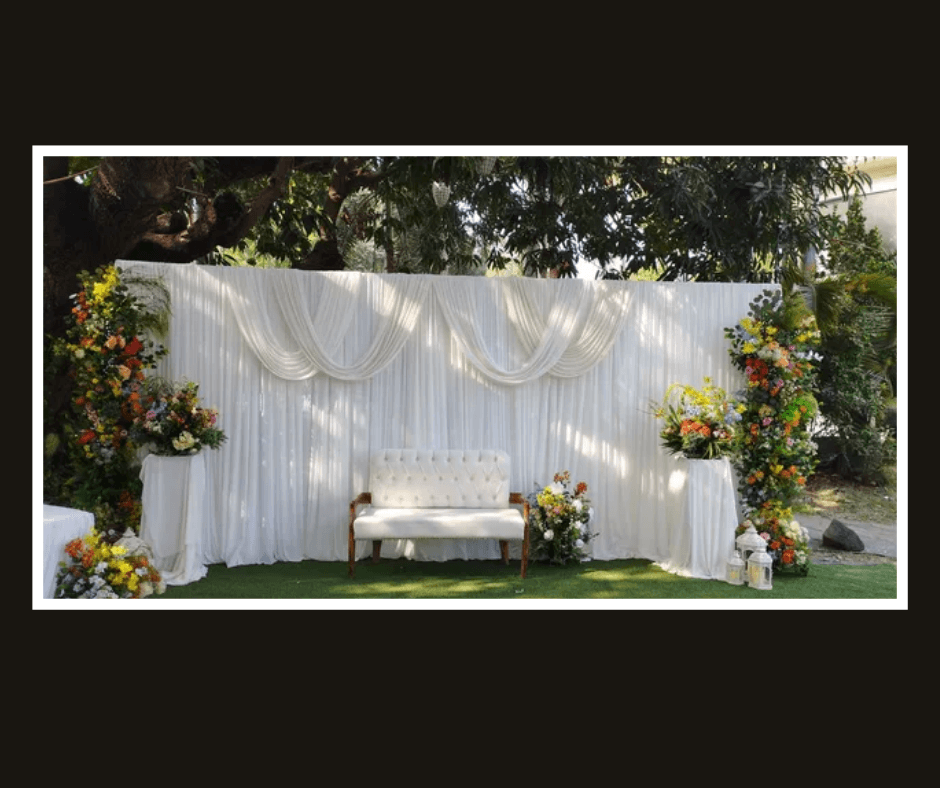 Wide white draped wall with colorful floral arrangements at both sides and a white bench