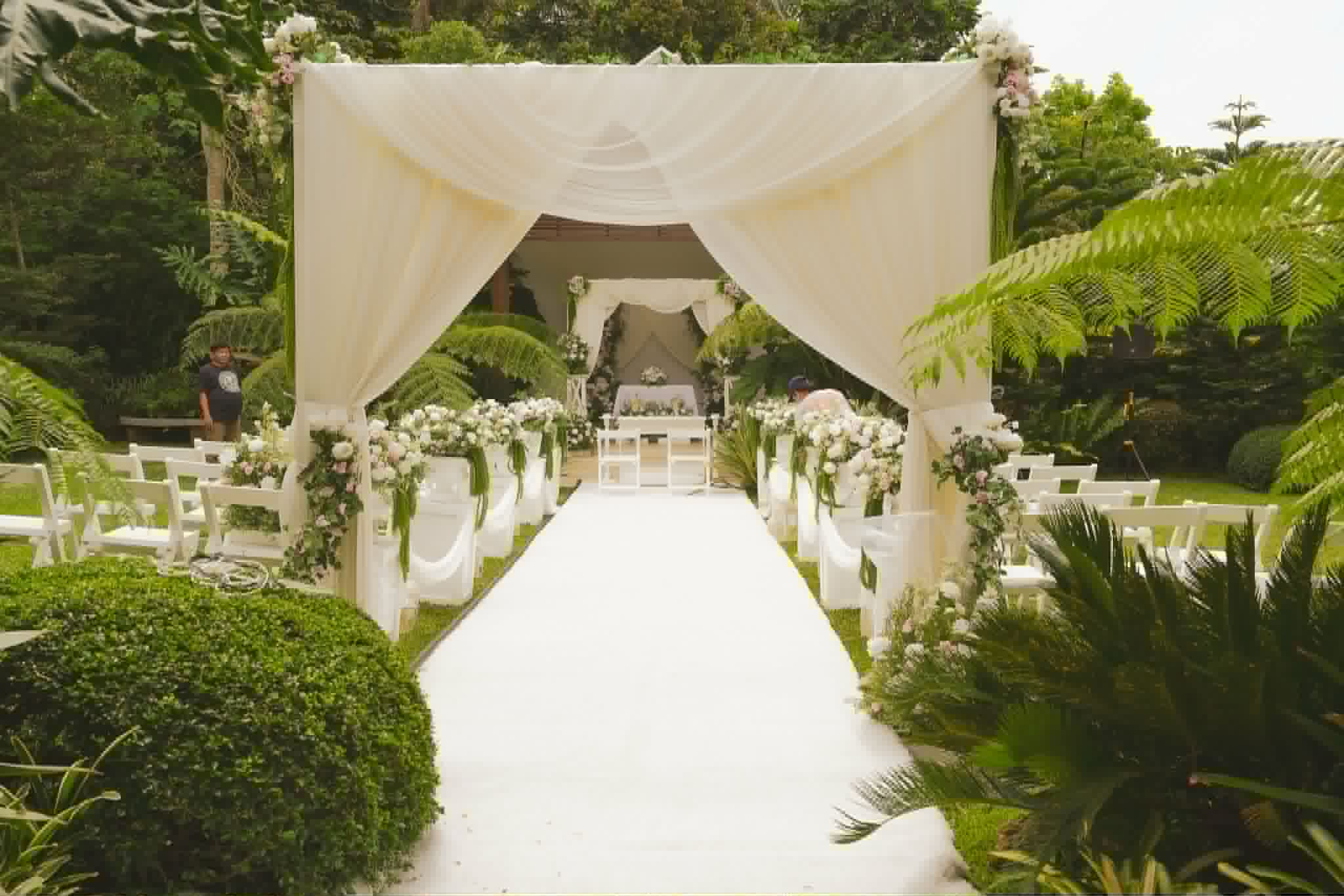 White draped garden wedding arch with flowers and a long white aisle