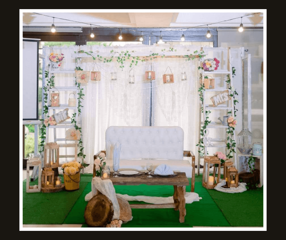 White draped photo gallery backdrop with suspended frames, flowers, greenery, and a white loveseat