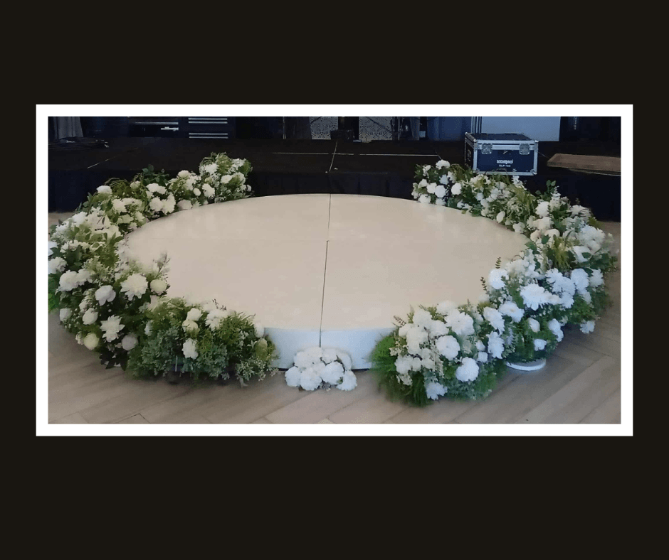 Circular white stage bordered by white flowers and greenery