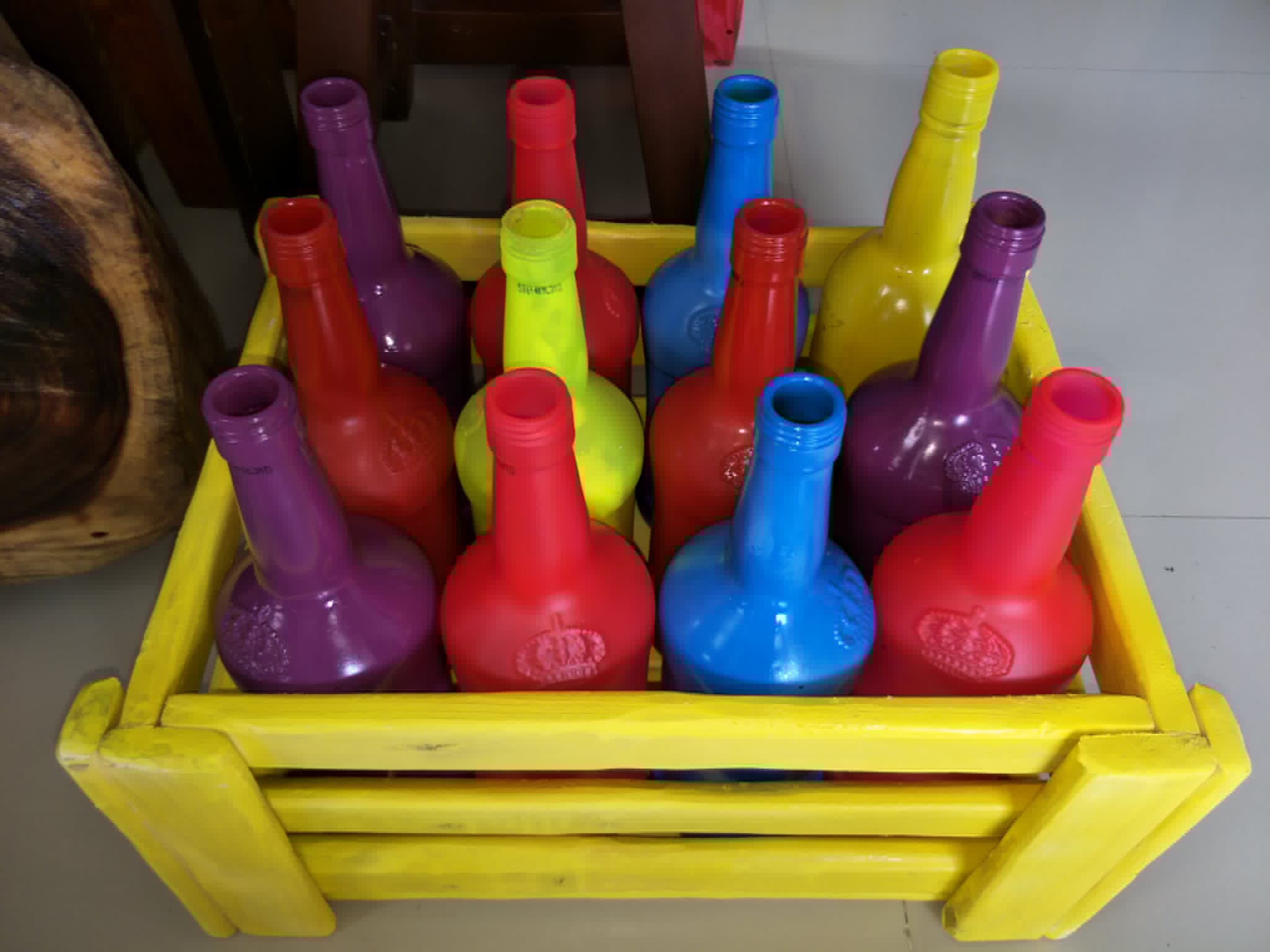 Brightly painted decorative bottles arranged in a yellow wooden crate
