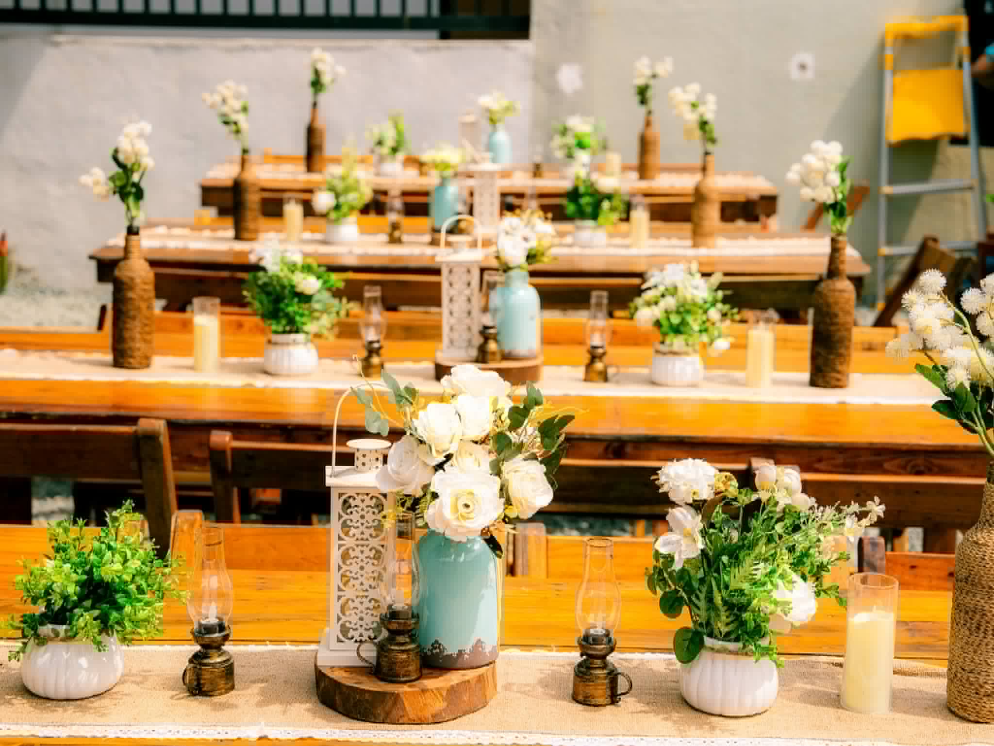 Rustic event tables styled with small bottles, flowers, and lanterns