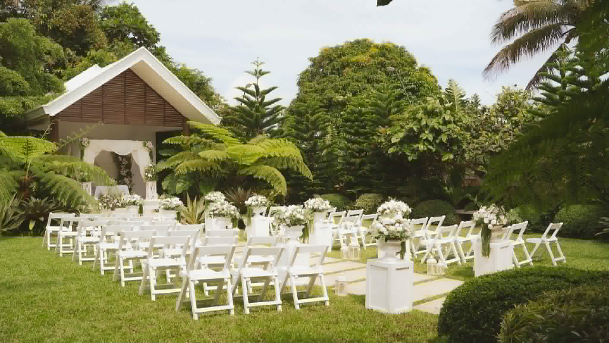 White wedding chairs arranged on a garden lawn facing a small chapel