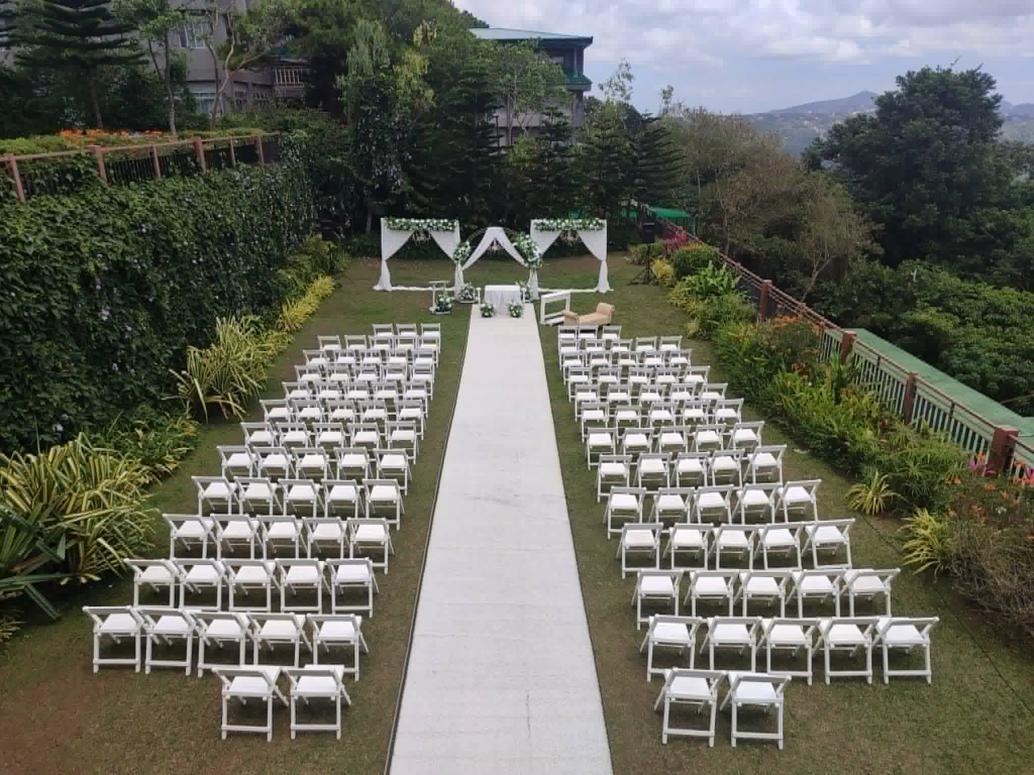 Large symmetrical outdoor ceremony layout with rows of white chairs and a central aisle