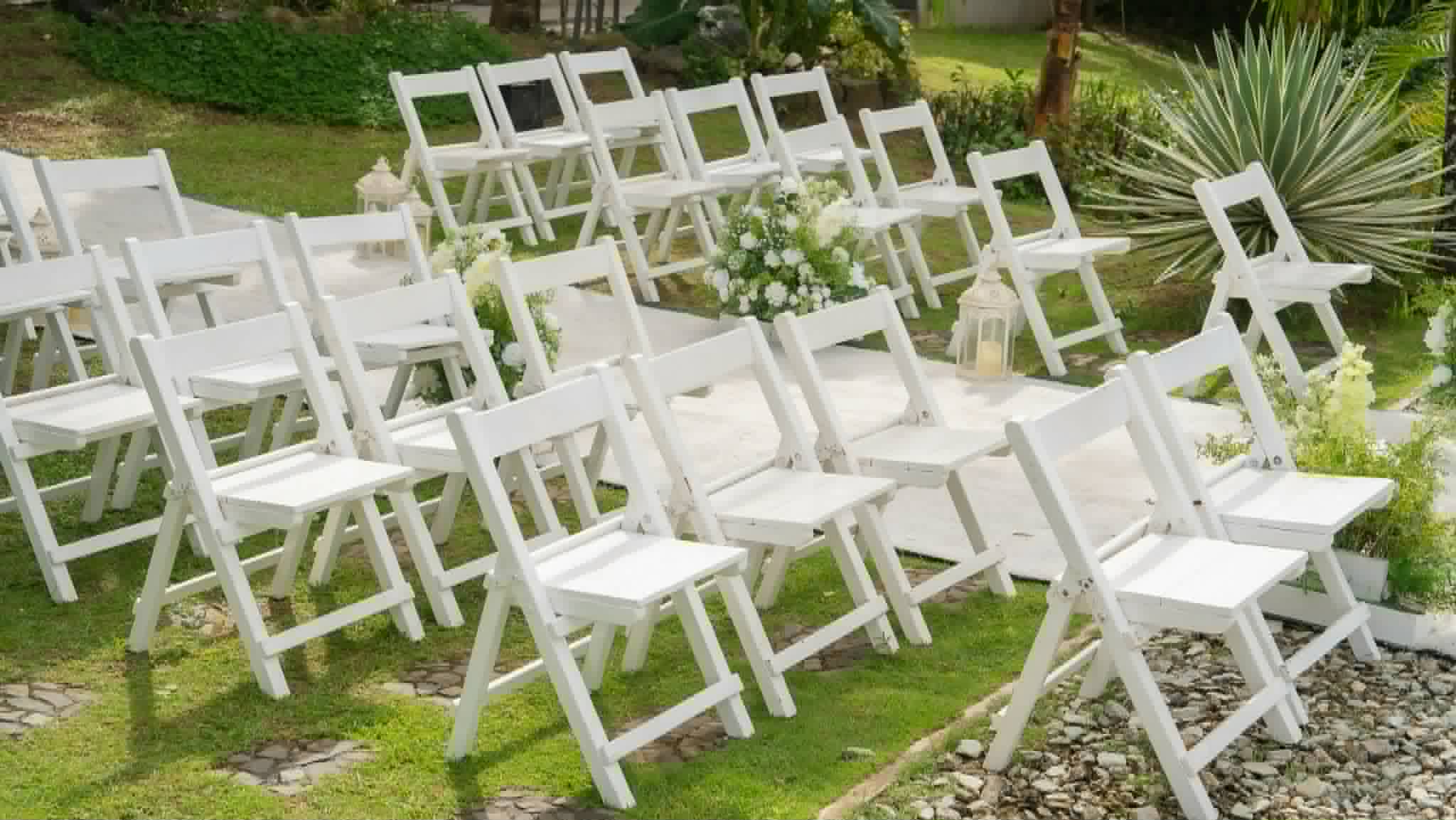 Rows of white folding chairs arranged on a garden lawn with aisle flowers