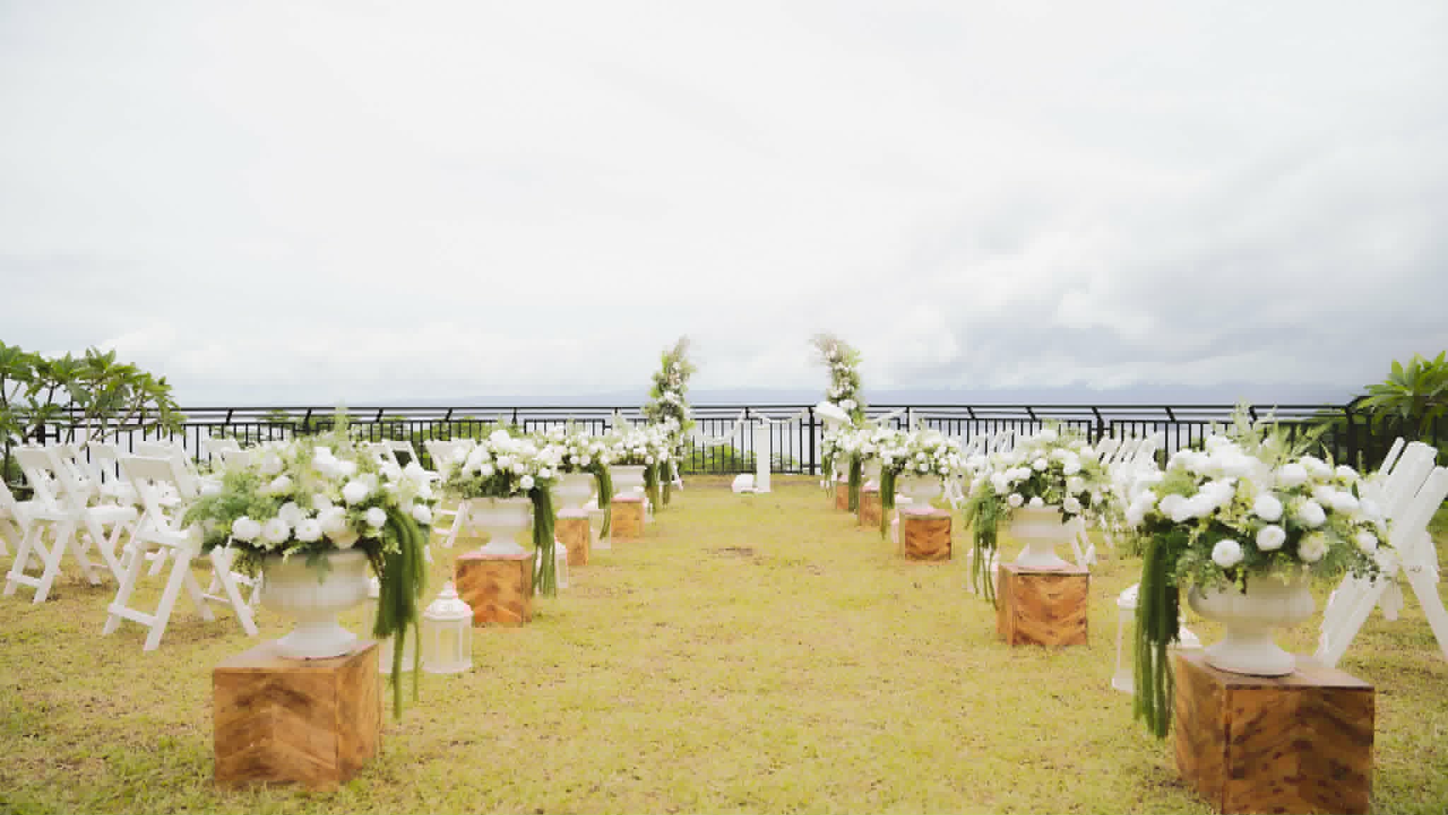 Outdoor wedding seating with white chairs and floral arrangements on wooden stump aisle markers