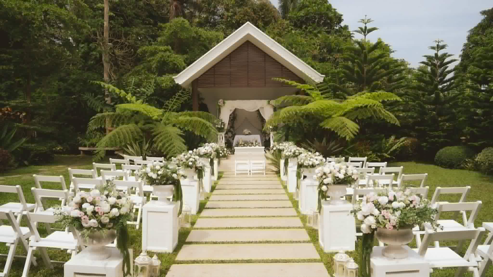 Symmetrical garden wedding aisle lined with white chairs and flowers leading to a chapel