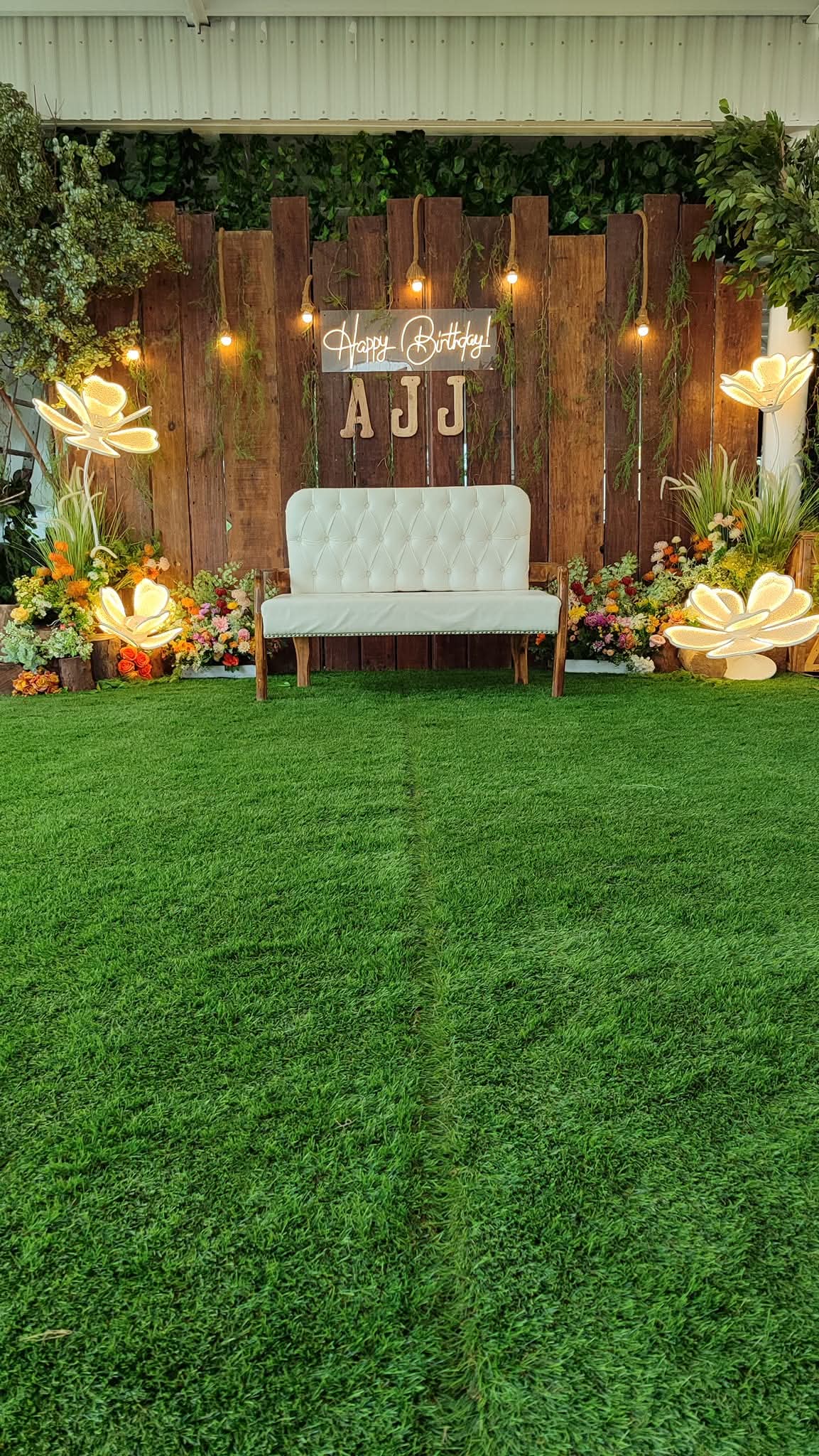 Tufted loveseat against a wood backdrop with a bloom wall and glowing flower lights