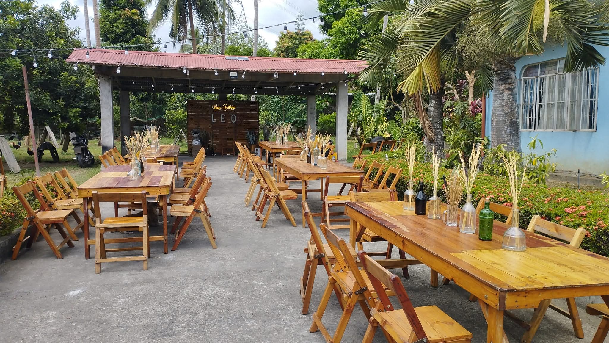 Rustic wooden tables with wheat-and-bottle centerpieces set outdoors