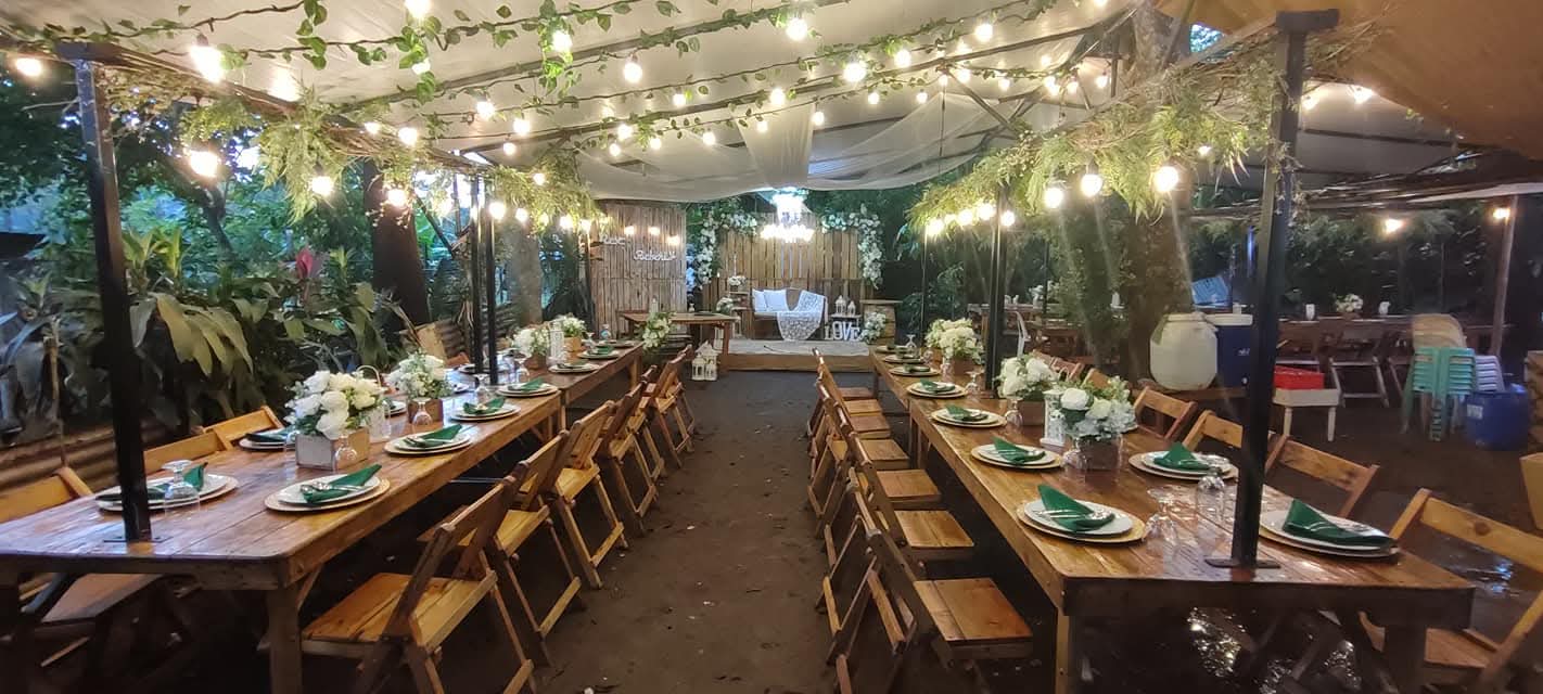 Long wooden reception tables set under string lights and hanging greenery
