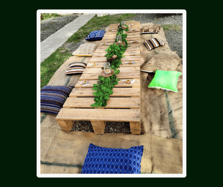 Long low pallet tables styled with greenery and colorful floor cushions