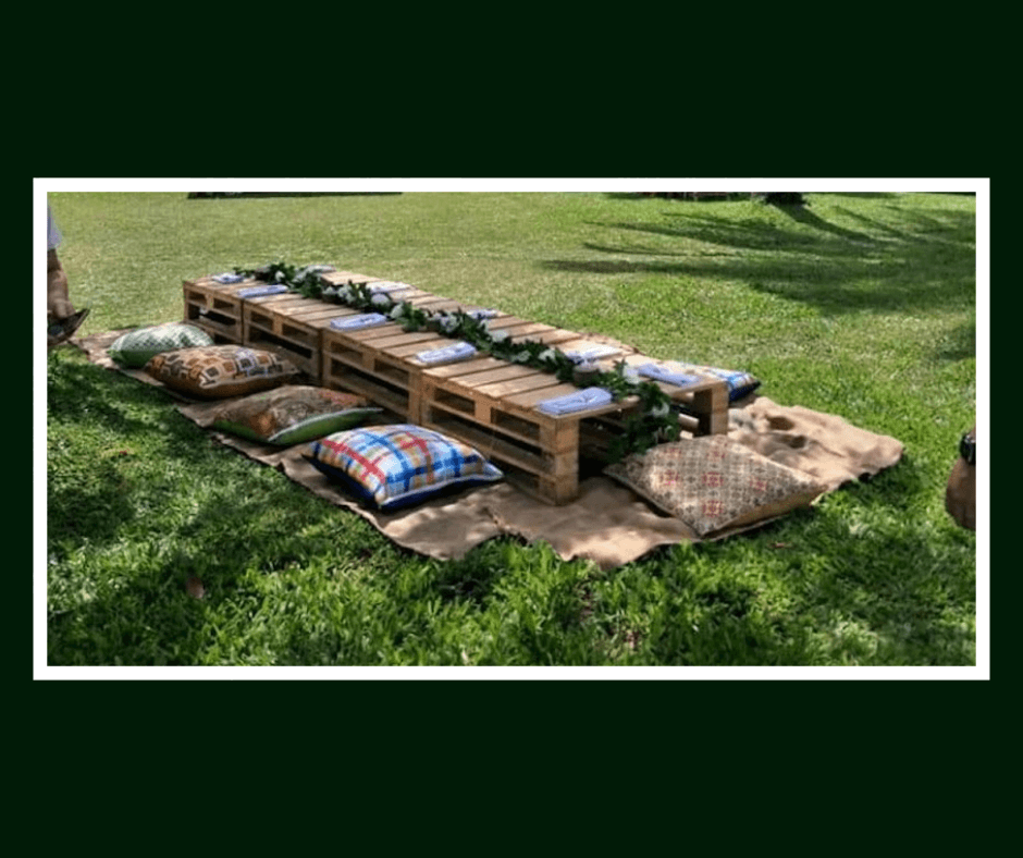 Long low pallet picnic table with neutral floor cushions on a lawn