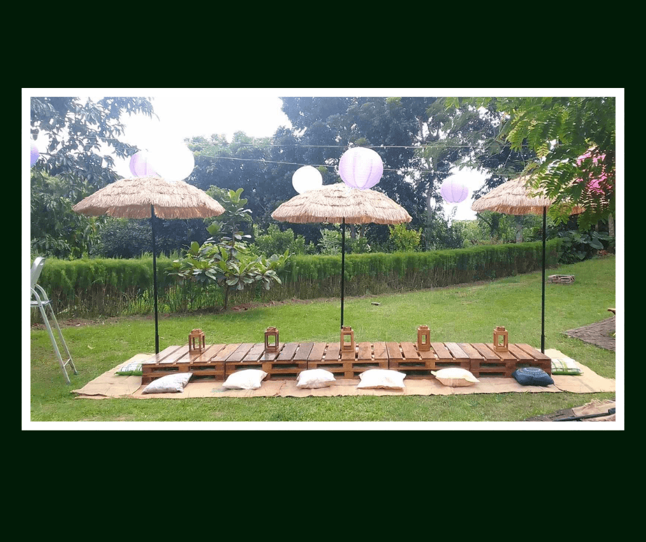 Low pallet picnic tables arranged beneath woven parasols on a lawn