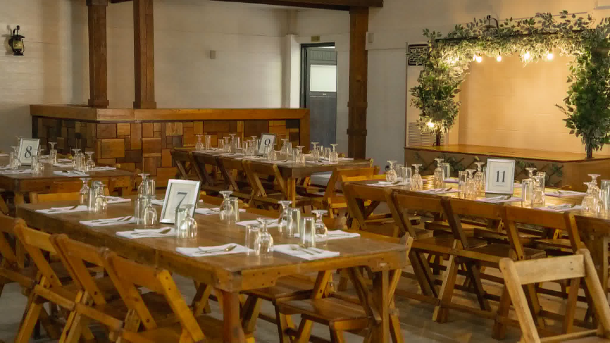 Formal reception layout with rustic wooden tables, chairs, place settings, and greenery