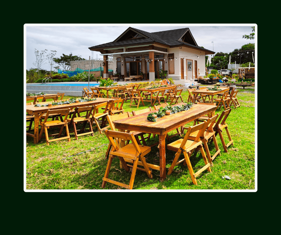 Rustic wooden banquet tables and chairs arranged on a garden lawn