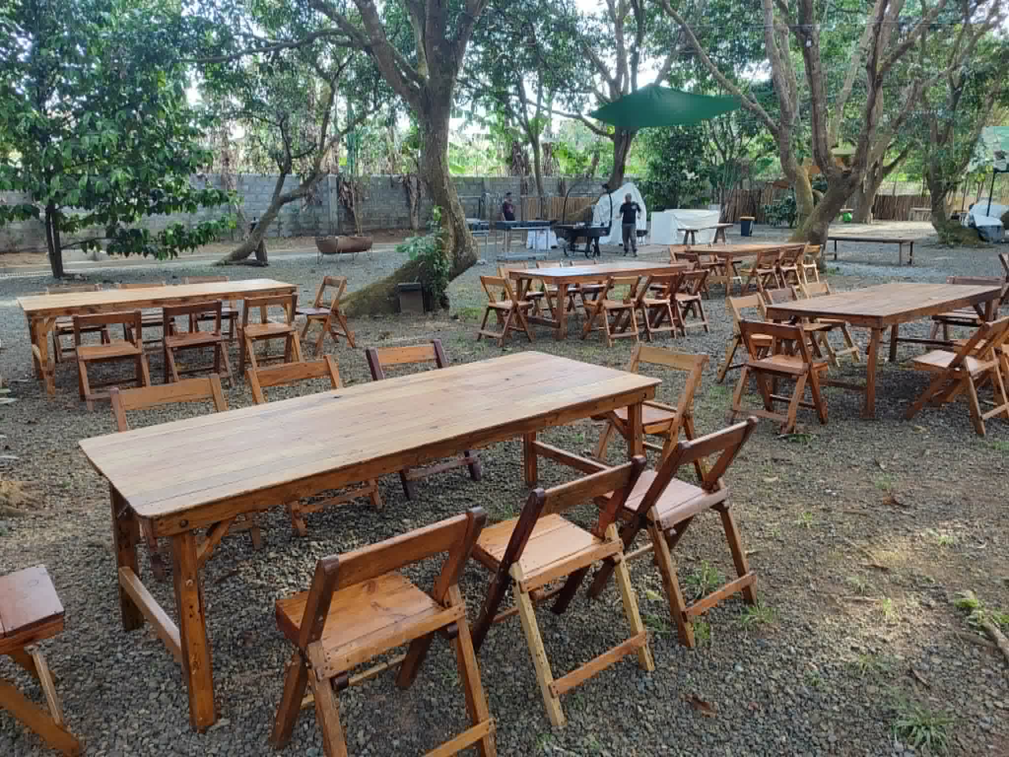 Rustic wooden tables and folding chairs arranged beneath garden trees