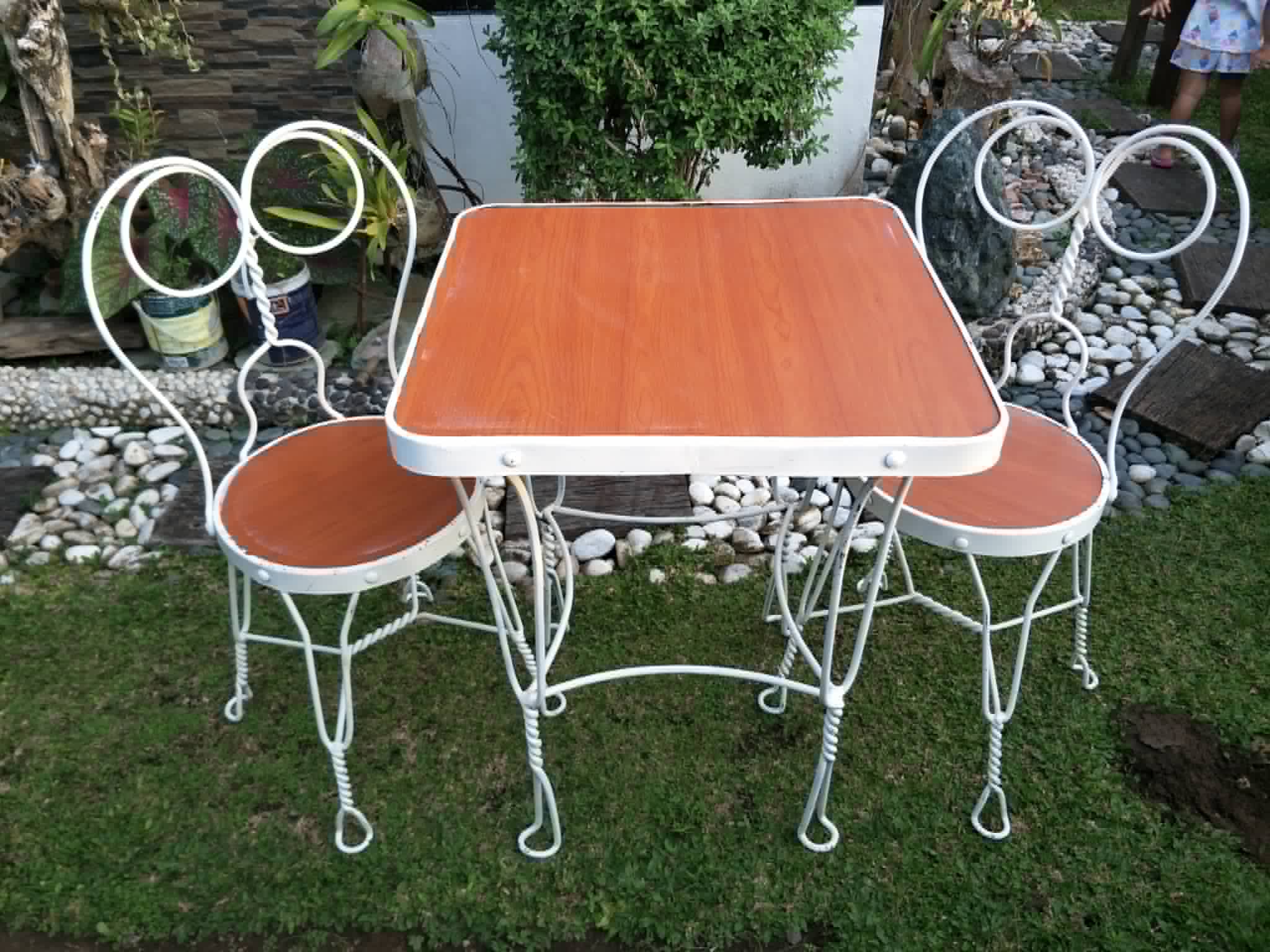 White scrollwork patio table with four matching chairs and wood-toned seats